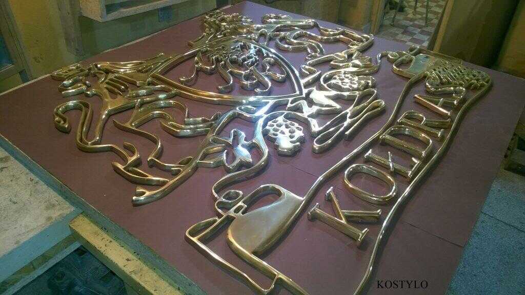 an angled close-up of luxurious bas-relief in the shape of an openwork crest with two lions wearing crowns polished to high gloss from brass by Kostylo atelier